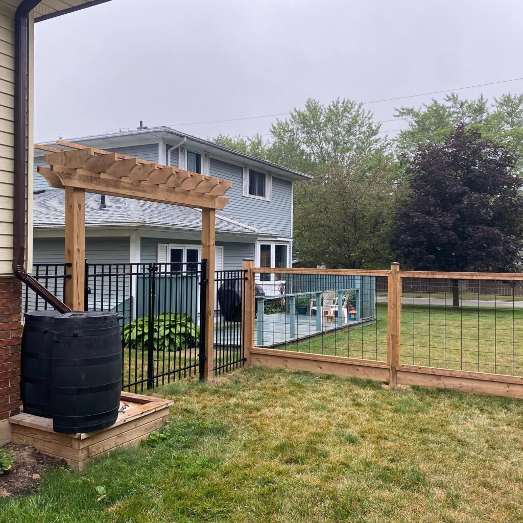 pergola over double iron gate attached to house and wood and wire fence down backyard property