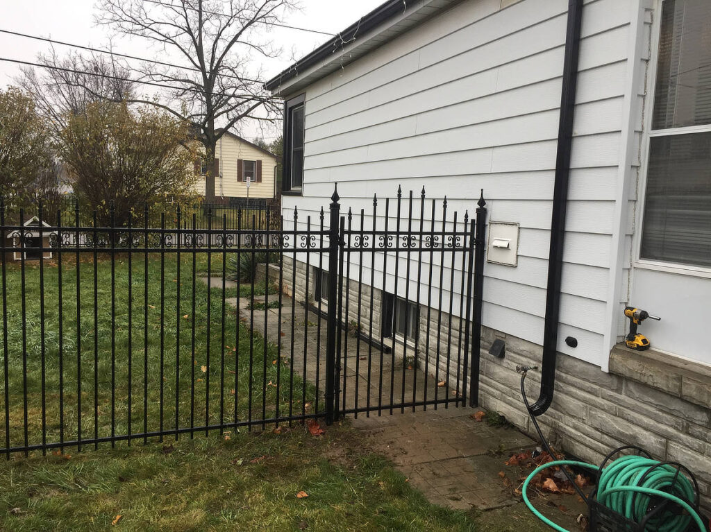 Decorative top wrought iron fence and gate attached to the side of a house