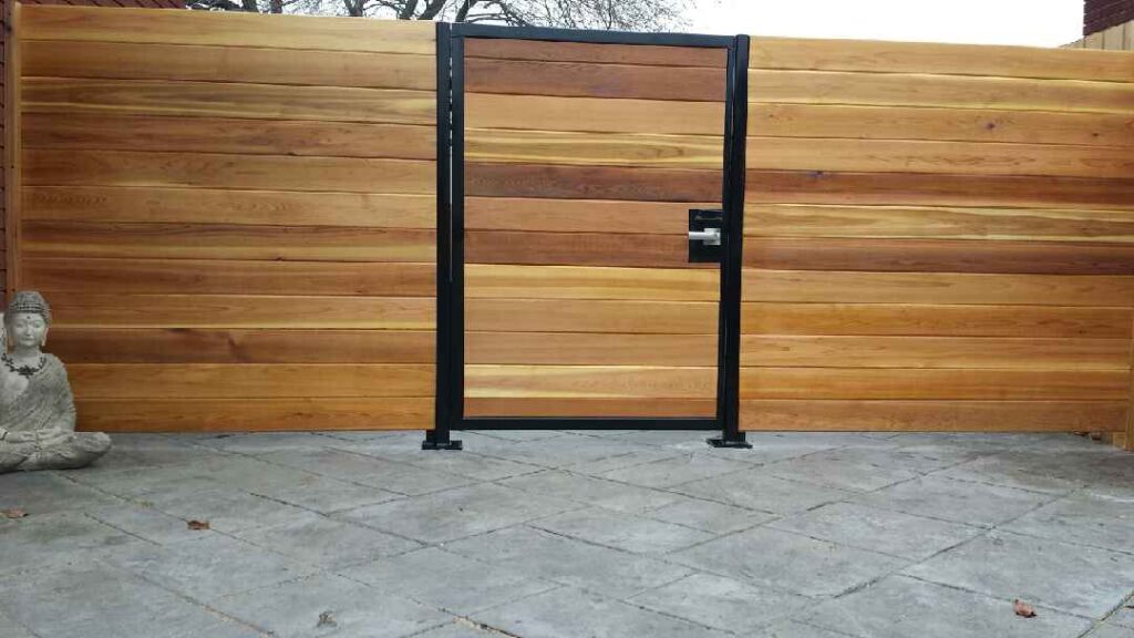A horizontal wood fence with black iron posts and silver door handle.