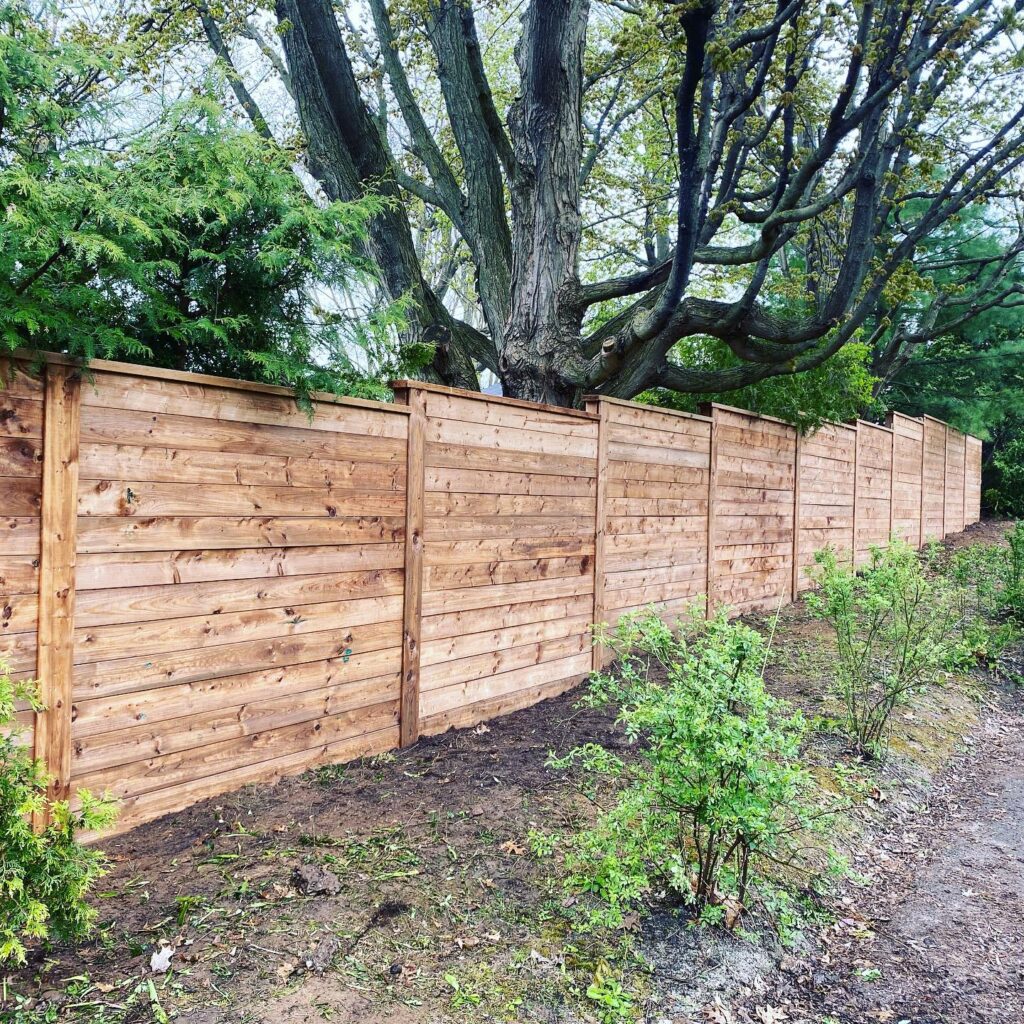 Stepped wood horizontal fence against large trees.
