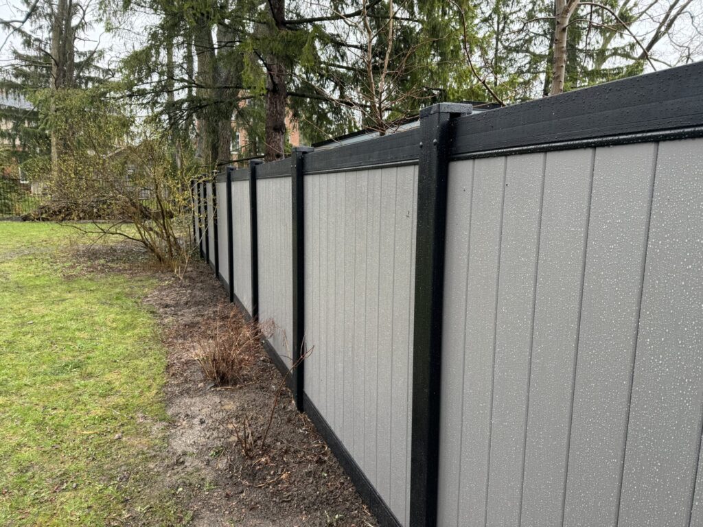 Side long down view of a vinyl fence with black posts and top and bottom rails
